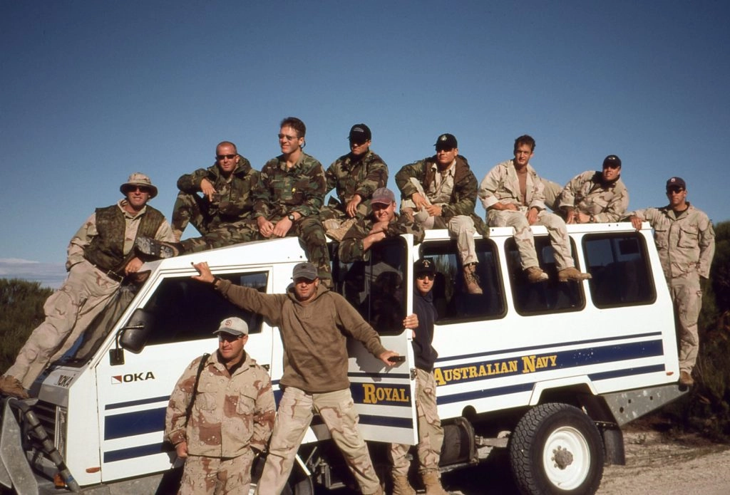 Group of people in military attire on and around a Royal Australian Navy vehicle, leadership and teamwork.